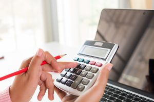 woman-hand-holding-red-pencil-working-with-calculator-scaled – מחושבים משכנתאות ופיננסים